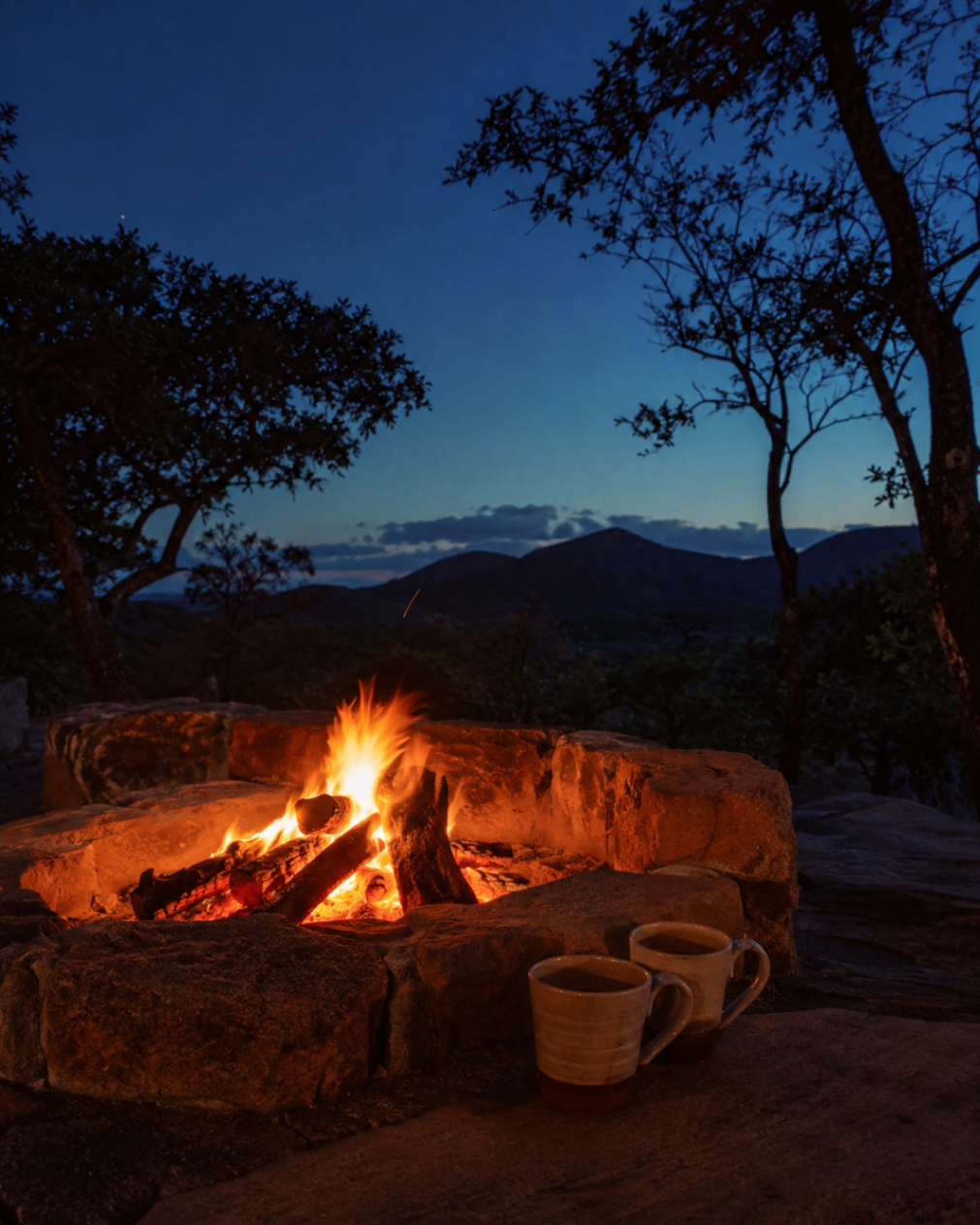 A glowing outdoor fire pit at dusk with mountain silhouettes beyond