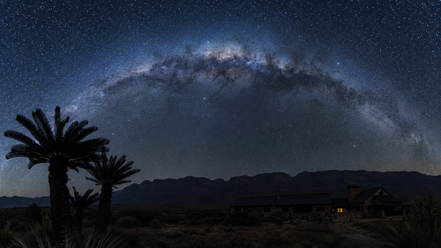 The Milky Way arching over the farmhouse and mountain ridge at night